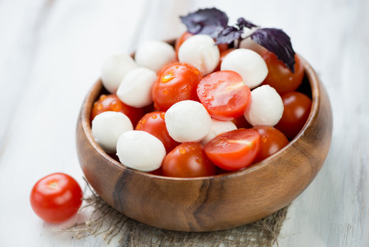 Red cherry tomatoes and mozzarella balls in a wooden bowl