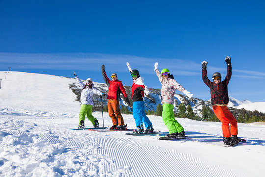 Skier and snowboarders in a row lifting hands up