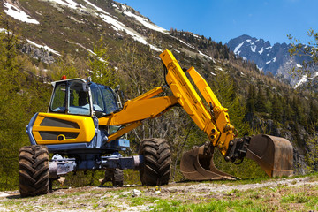 Yellow excavator working near mountains