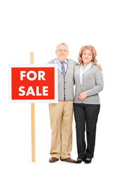 Fototapeta premium Mature husband and wife standing by for sale sign