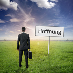 Mann steht im Gras mit Schild Hoffnung