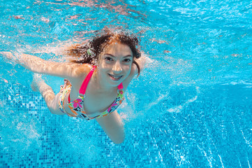 Obraz na płótnie Canvas Happy active underwater girl swims in pool and having fun