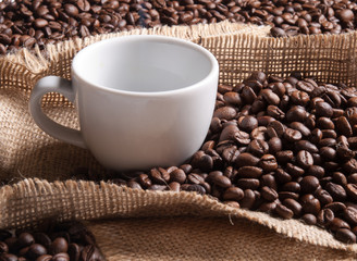 white cup with coffee on burlap background with beans