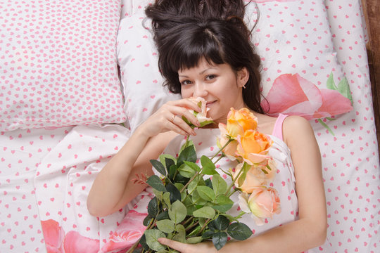 Beautiful girl enjoying scent of flowers in bed