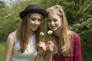 Fototapeta premium Two teenage girls blowing seeds from the Dandelion plant