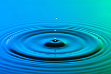Water drop close up with concentric ripples colourful blue and g - 64588024