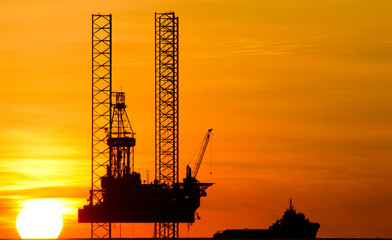 Offshore drilling rig and supply vessel at sunset