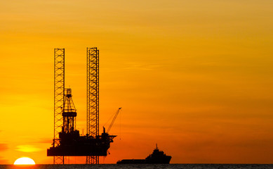 Offshore drilling rig and supply vessel at sunset