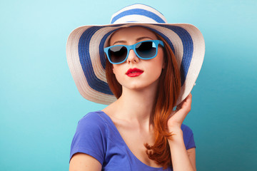 Redhead girl with sunglasses and hat on blue background.
