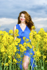 Naklejka na ściany i meble Beautiful young woman in blue dress in yellow field