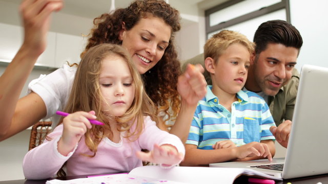 Happy children drawing at the table with their parents and using