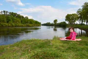 Little girl sitting near the river.