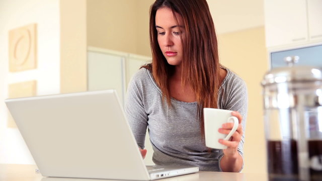 Pretty brunette sitting using laptop and drinking coffee