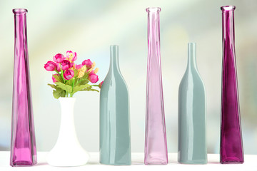Different decorative vases on shelf on light background
