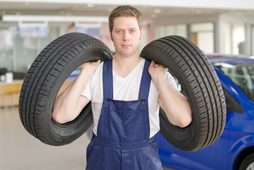 Young mechanic with tires in service center.