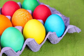 Colorful Easter eggs in tray on wooden background
