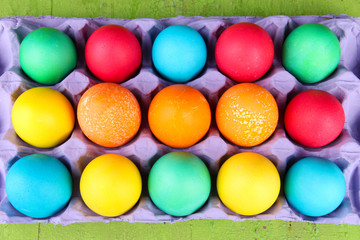 Colorful Easter eggs in tray on wooden background