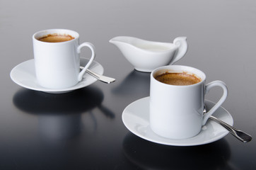 Two cups of coffee with a milk jug