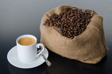 A cup of coffee with coffee beans in a burlap bag