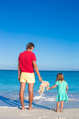 Dad with little daughter holding bunny toy on caribbean beach