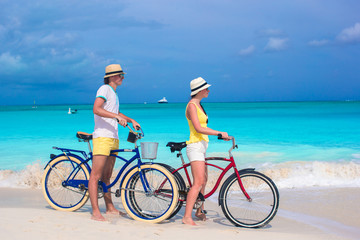 Fototapeta premium Young happy couple riding bikes on white tropical beach