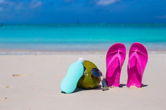 Flip flops, coconut and suncream on white sand