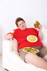 Fat man eating tasty sandwich on home interior background