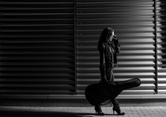young woman in black jacket with guitar at night station