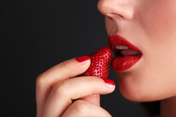 Girl with red lips, nails and strawberries on dark background