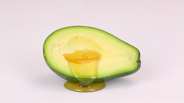 Oil drops over a half cut avocado on a white background