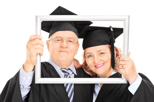 Mature graduates posing behind a picture frame