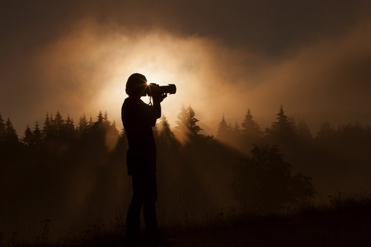 silhouette of woman photographer taking photos in forest with fo