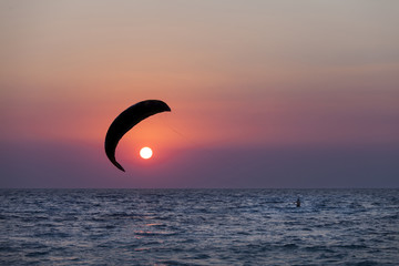 Silhouette of a kitesurfer sailing at sunset