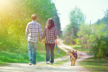 Young couple holding hands and walking with their dog in the vil