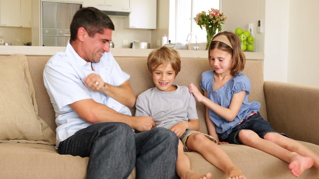Father and daughter tickling son in the couch