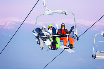 Three smiling snowboarders sitting on ropeway