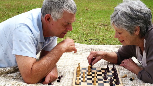 Senior couple relaxing in the park lying on a blanket playing ch