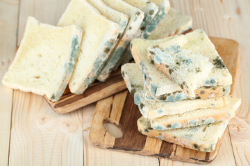 Mouldy bread on cutting board, on wooden background