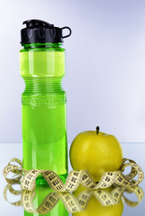 Sports bottle, apple and measuring tape on grey background