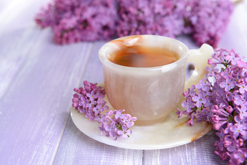 Fototapeta na wymiar Beautiful lilac flowers with cup of tea on table close-up