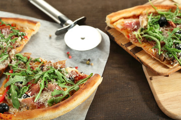 Pizza with arugula on cutting board, on color wooden background