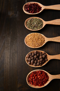 Different spices in spoons on wooden background