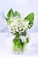 Beautiful lilies of the valley in glass vase on wooden table