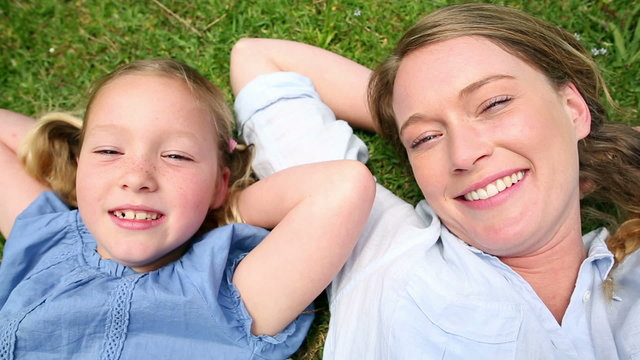 Happy mother lying on the grass with her little girl in the park