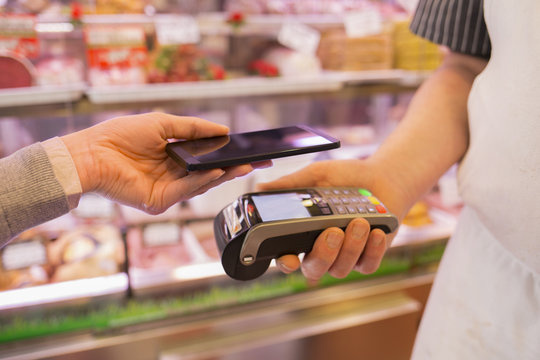 Woman Paying With NFC Technology On Mobile Phone, In Supermarket