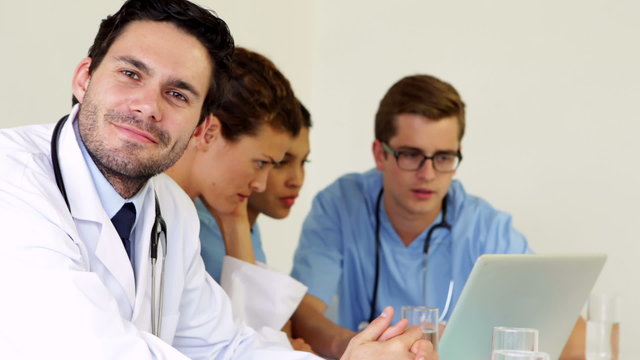 Doctor smiling at camera while colleagues are talking