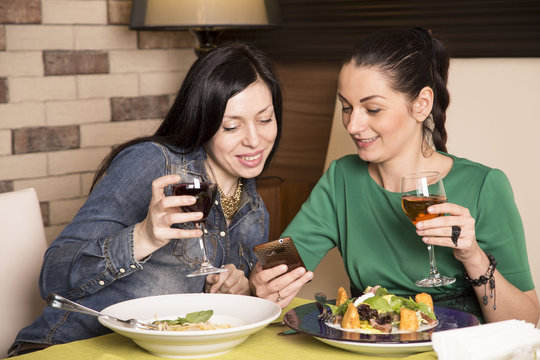 Two women using a smart phone. At restaurant during a dinner
