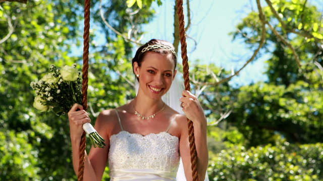 Happy bride sitting on a swing looking at camera