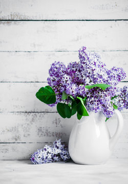 Lilacs in white vase on rustic background