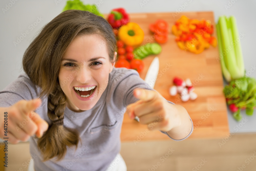 Wall mural happy young housewife in kitchen pointing in camera